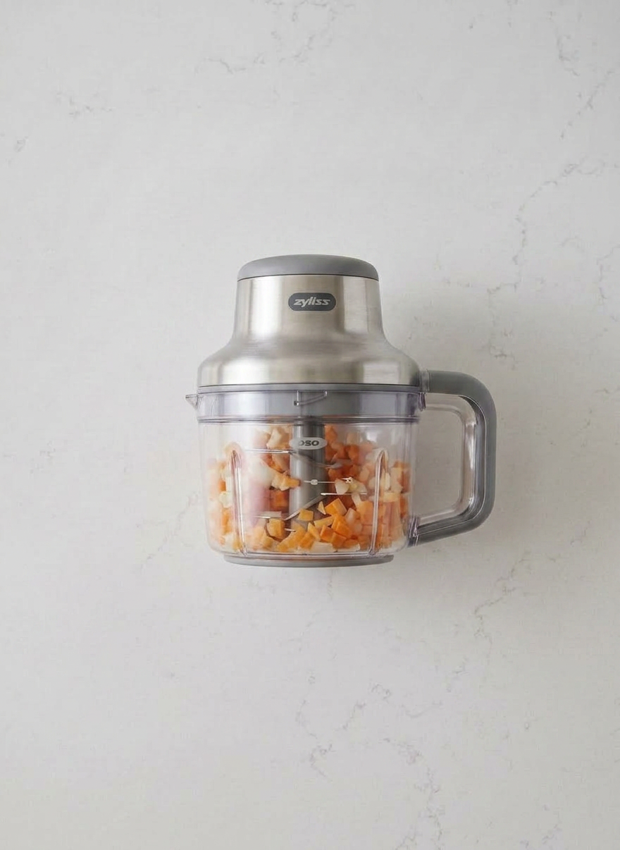 Ingredients prepped for homemade broth Pot with simmering broth containing carrots, onions, bay leaf, and peppercorns alongside a small bowl of salt, wooden spoon, and food processor with chopped vegetables
